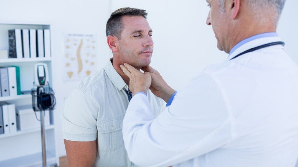 A doctor presses gently along a patient's neck during an auto injury assessment in a bright clinic exam room