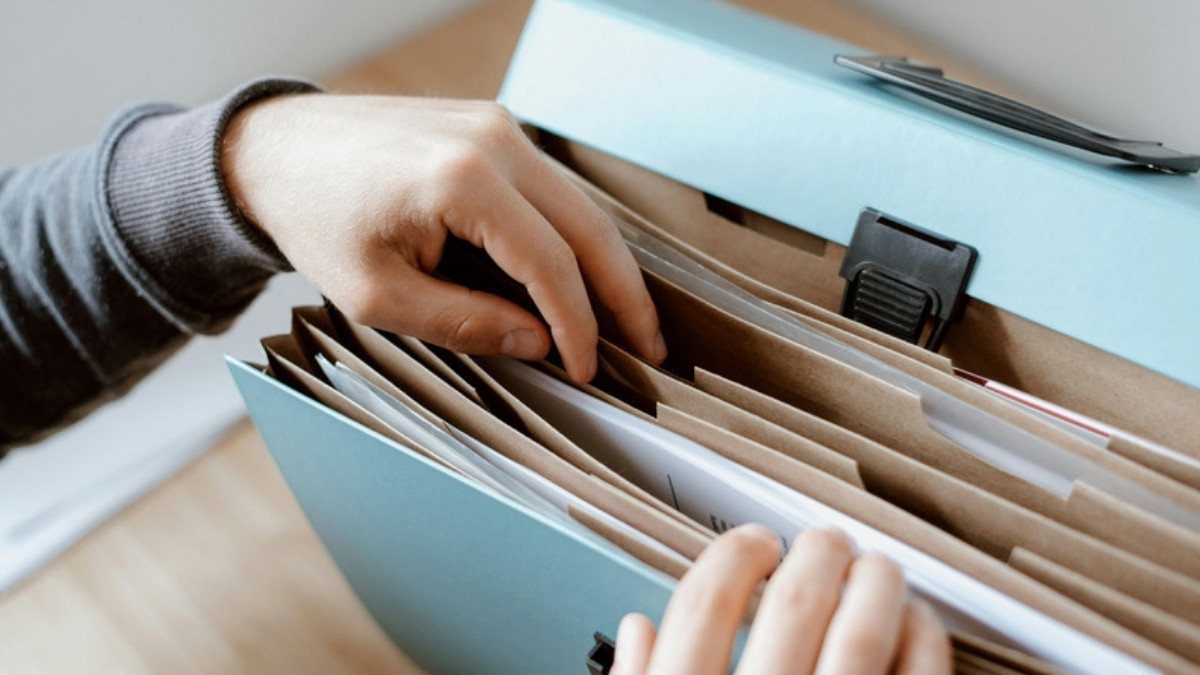 Hands flip through an accordion file of papers, gathering the records from an auto injury assessment and the visits after it