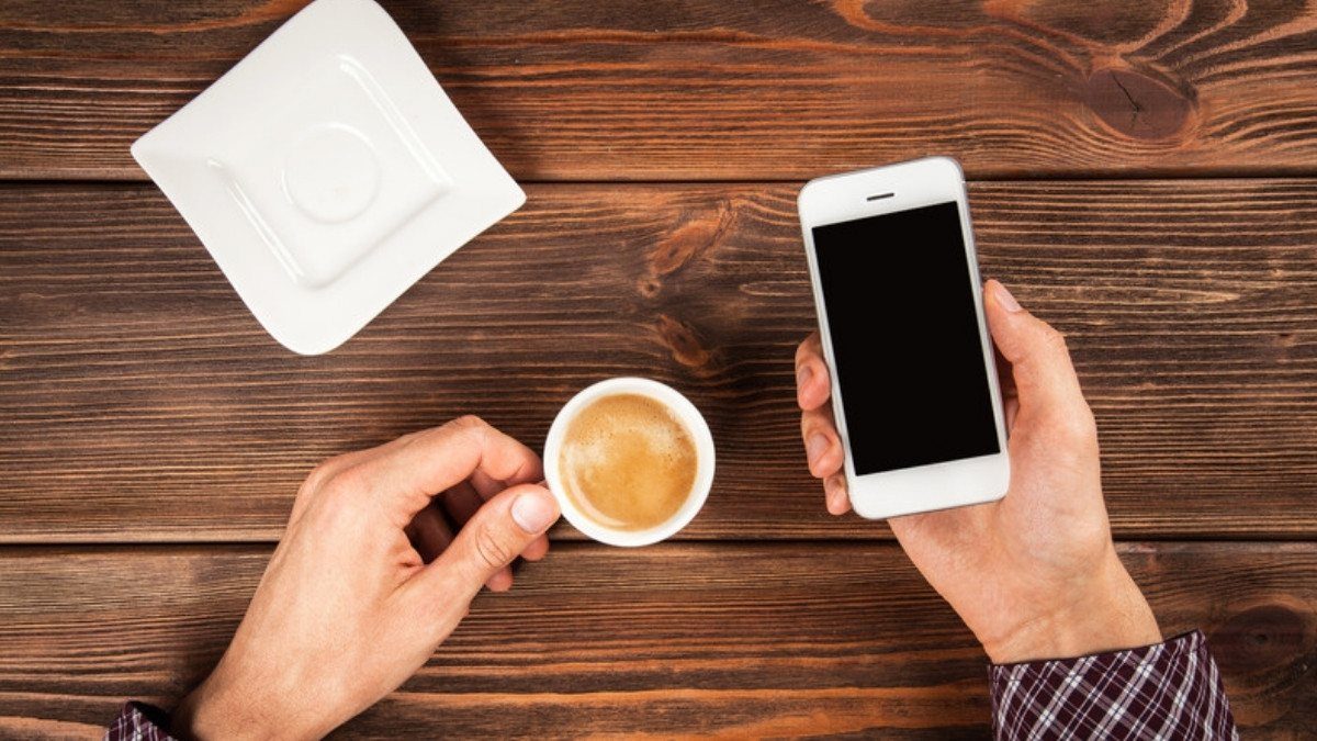 Hands hold a phone and a coffee cup over a wooden table, ready to share crash photos when no police report exists