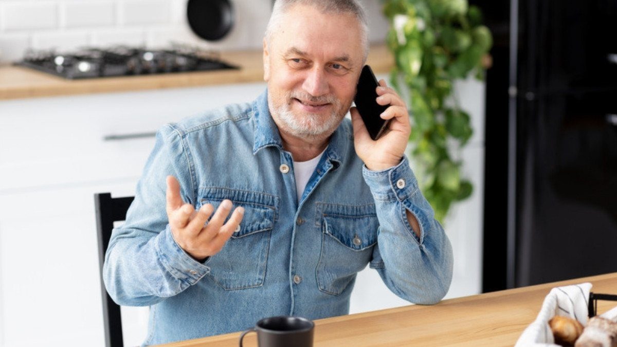 A gray haired man gestures on a phone call at his kitchen table, a simple way to reach car accident lawyers in Berkeley County