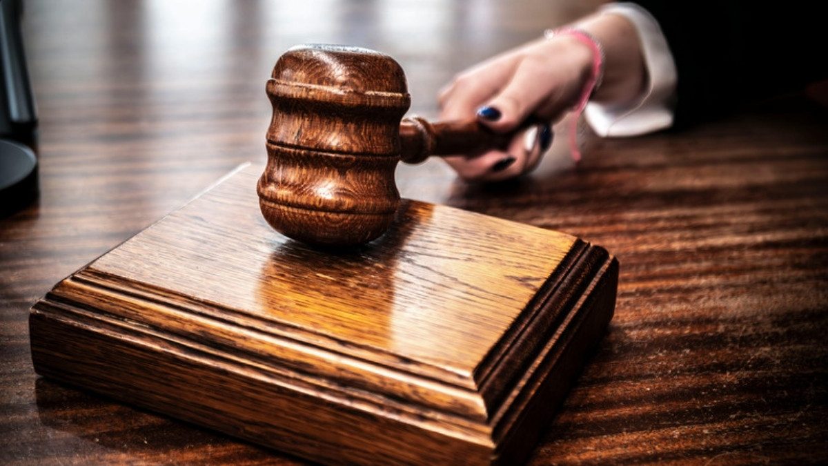 A hand holds a wooden gavel above its sound block on a dark wooden desk.