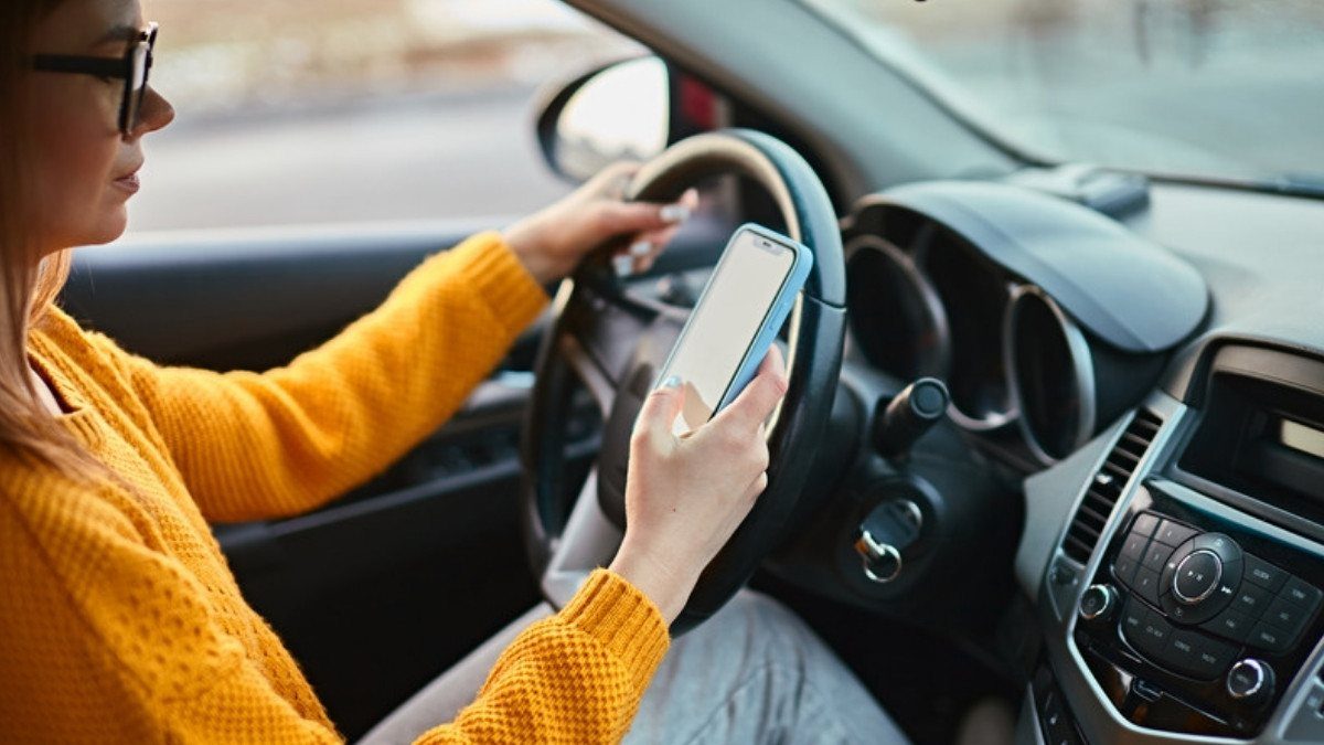 A driver in a yellow sweater reads her phone while steering, the habit distracted driving accident lawyers in Summerville look for