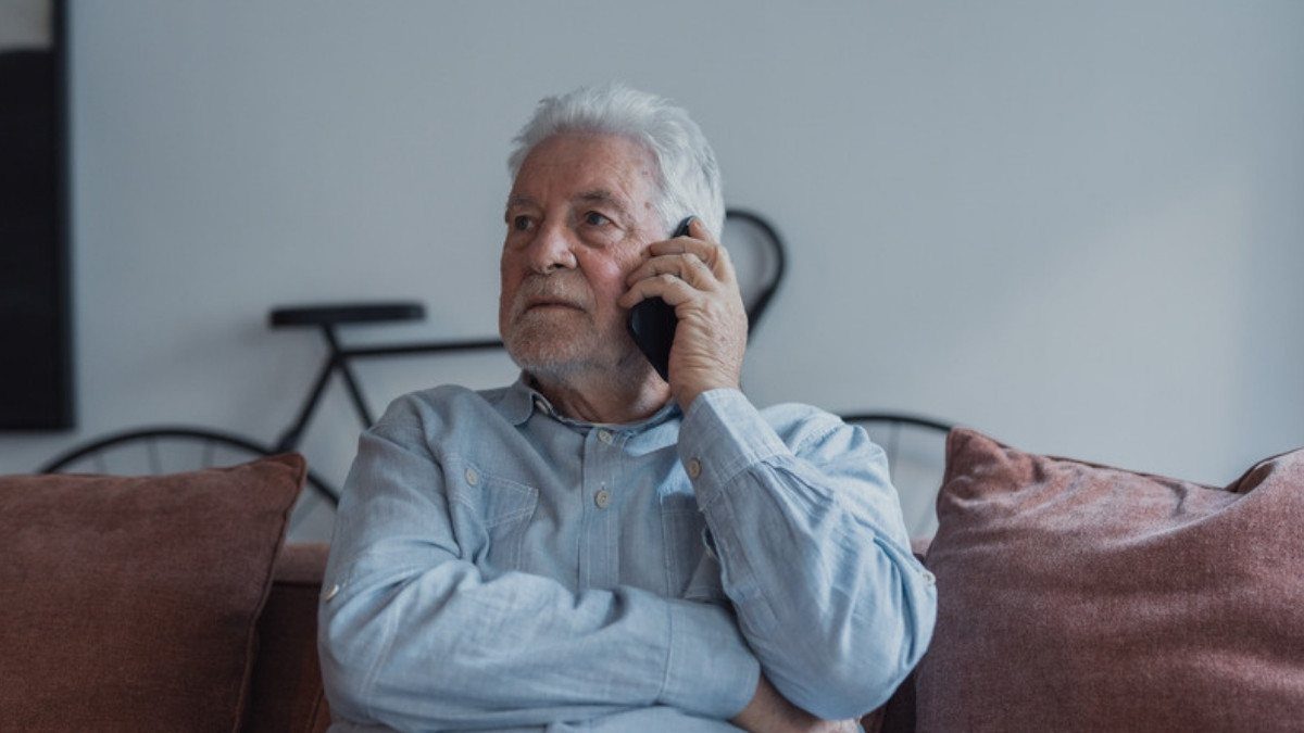 A gray haired man sits on his sofa with a phone to his ear, the kind of first call fatal car accident lawyers in Summerville take