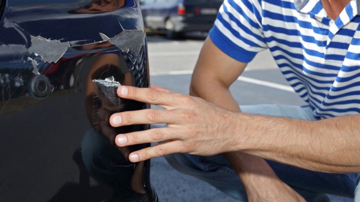 A man touches fresh scrapes on a parked car, the kind of damage hit and run accident lawyers in Summerville see after a driver leaves