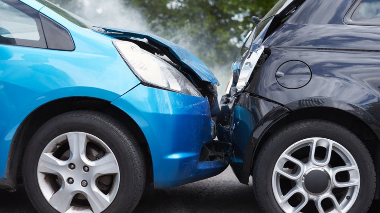A small blue car with a crumpled hood sits jammed against a dark car as steam rises after a collision.