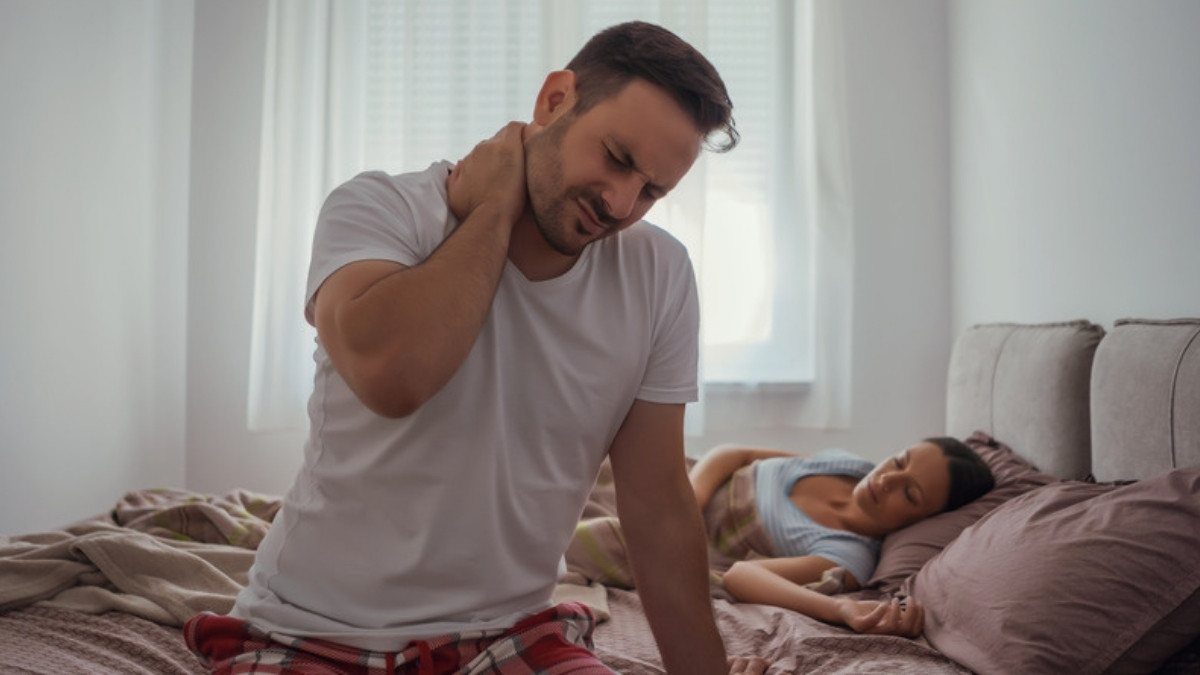 A man sits on the edge of his bed rubbing a stiff neck, pain that may surface days later and become part of an injury claim