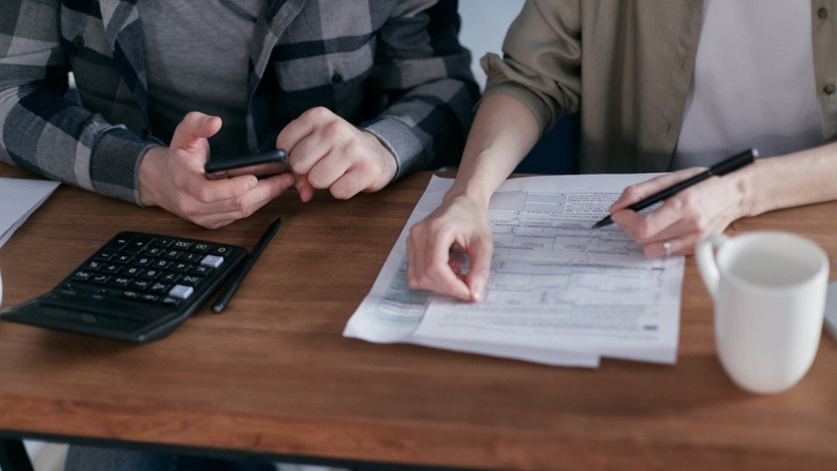 Two people review bills at a wooden table with a calculator and phone, adding up the losses in a car accident case