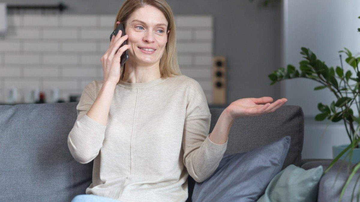 A woman on a gray couch gestures as she talks on her phone at home, sorting out questions about who was at fault