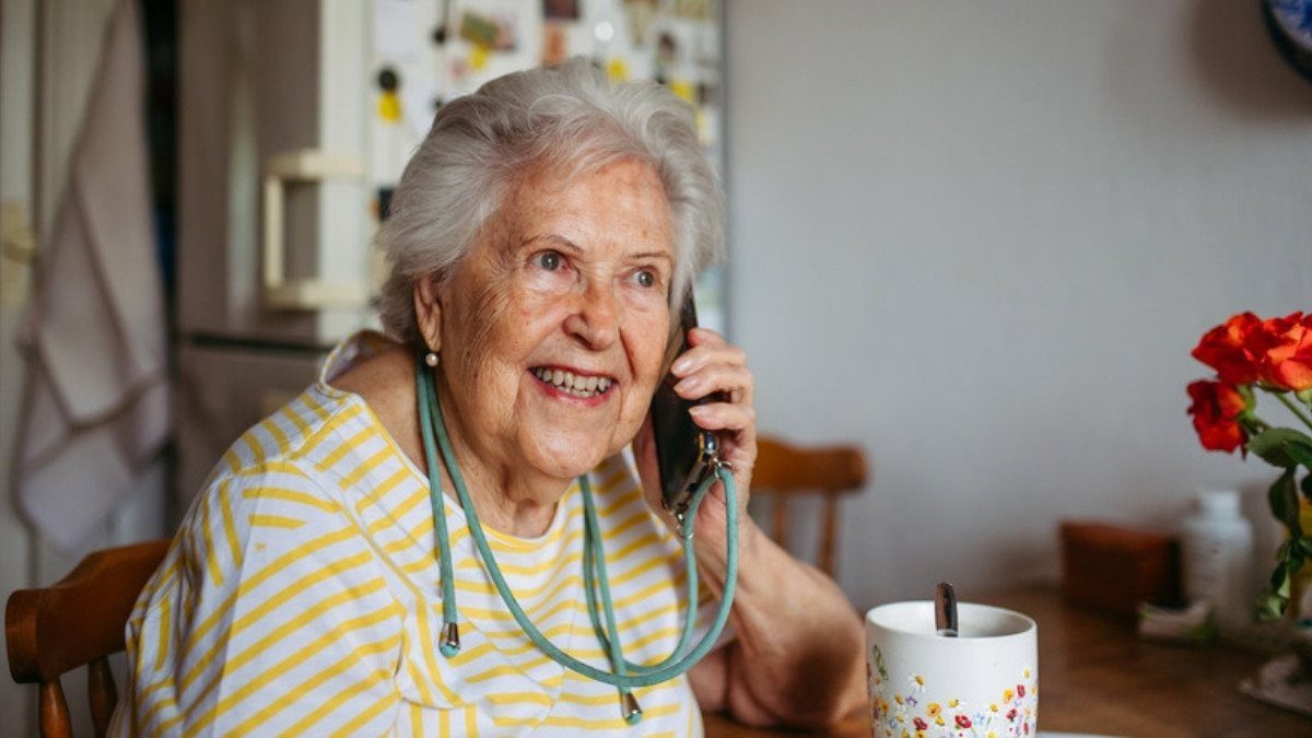 An older woman smiles during a phone call at her kitchen table, where a quick question for Ladson car accident lawyers can start