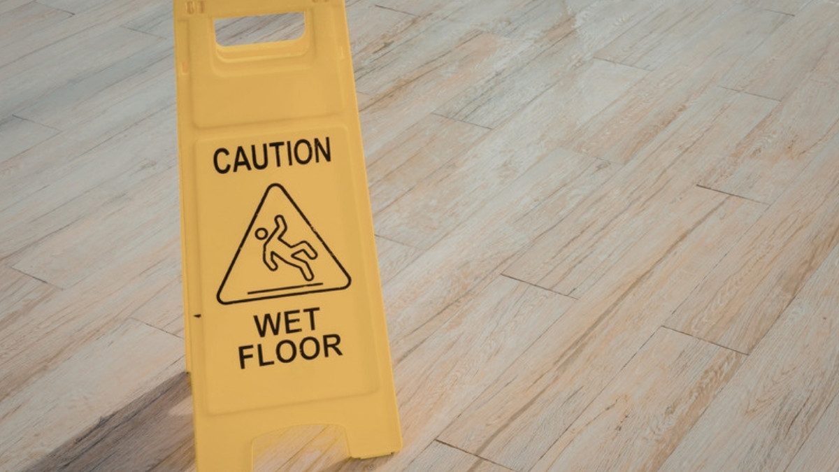 A yellow caution wet floor sign stands on a polished wooden floor.