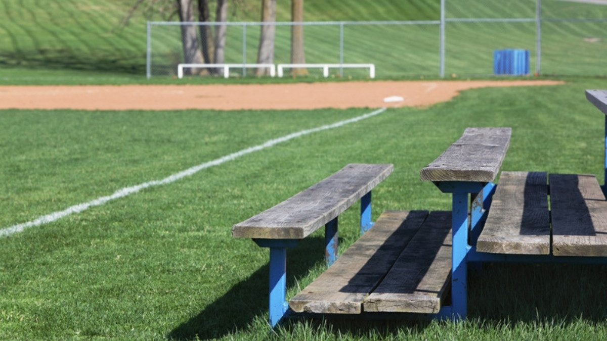 Weathered wooden bleachers with blue metal frames sit on the grass beside a baseball infield.