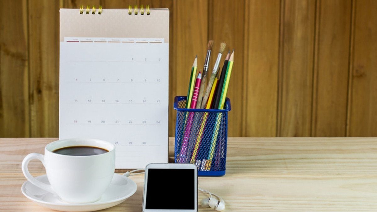 A desk calendar, coffee cup and phone sit on a wooden table, handy for booking time with Moncks Corner car accident lawyers