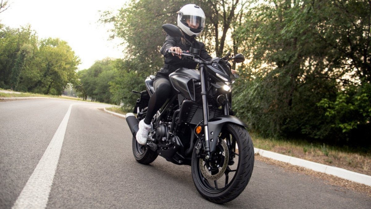 A rider in a white helmet rounds a tree lined road on a black motorcycle, a ride motorcycle accident attorneys in Summerville know well
