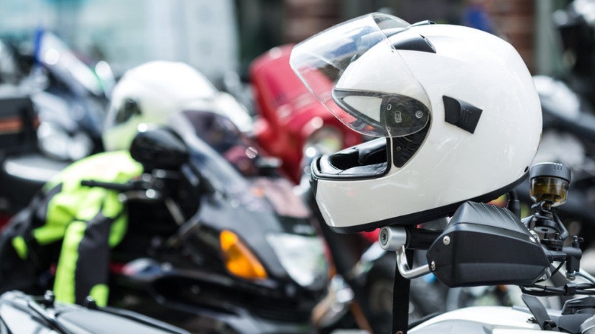 A white full face helmet hangs from the mirror of a parked motorcycle in a crowded lot of bikes