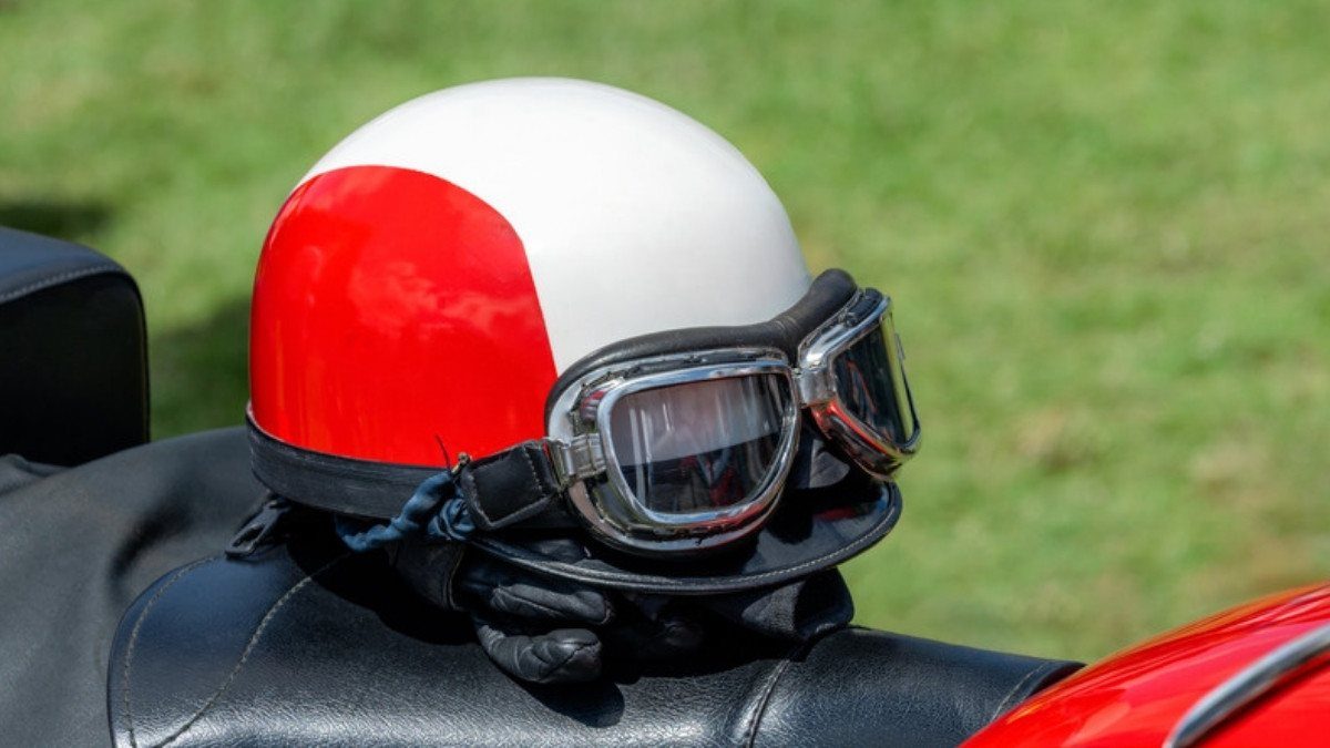 A red and white half helmet with goggles rests on a motorcycle seat, gear motorcycle helmet law injury lawyers in Summerville discuss
