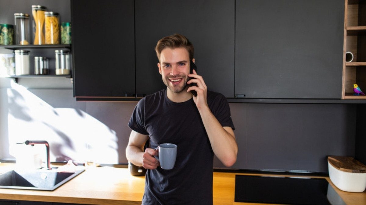 A young man with a mug smiles on a call in his kitchen, the kind of call motorcycle helmet law injury lawyers in Summerville welcome