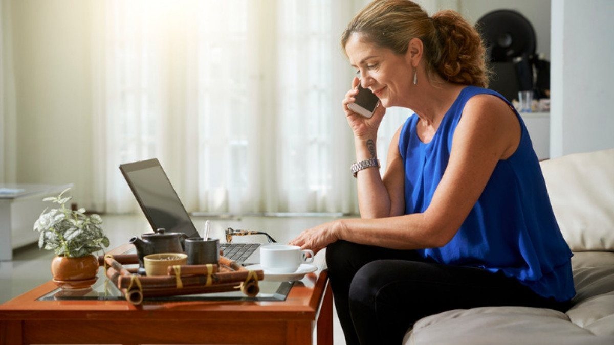 A woman makes a call from a sunlit sofa with tea and a laptop nearby, the sort of call North Charleston personal injury lawyers get