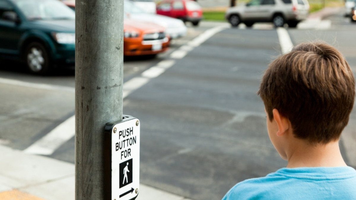 A boy waits at the crosswalk button as cars roll through the intersection, a moment pedestrian accident attorneys in Summerville study