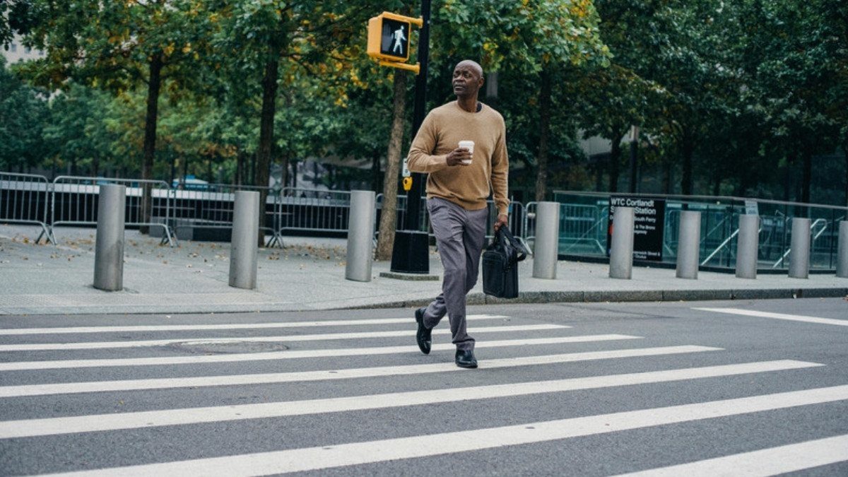A man with a coffee crosses a striped crosswalk under a walk signal, a trip pedestrian accident attorneys in Summerville know well