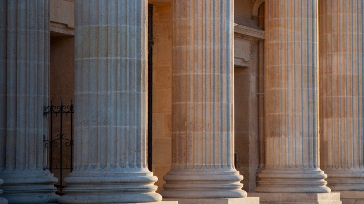 Sunlight warms a row of fluted stone columns along the entrance of a classical courthouse building