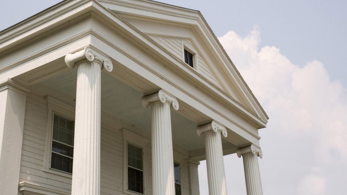 Tall white columns support the pediment of an old courthouse under a soft cloudy sky