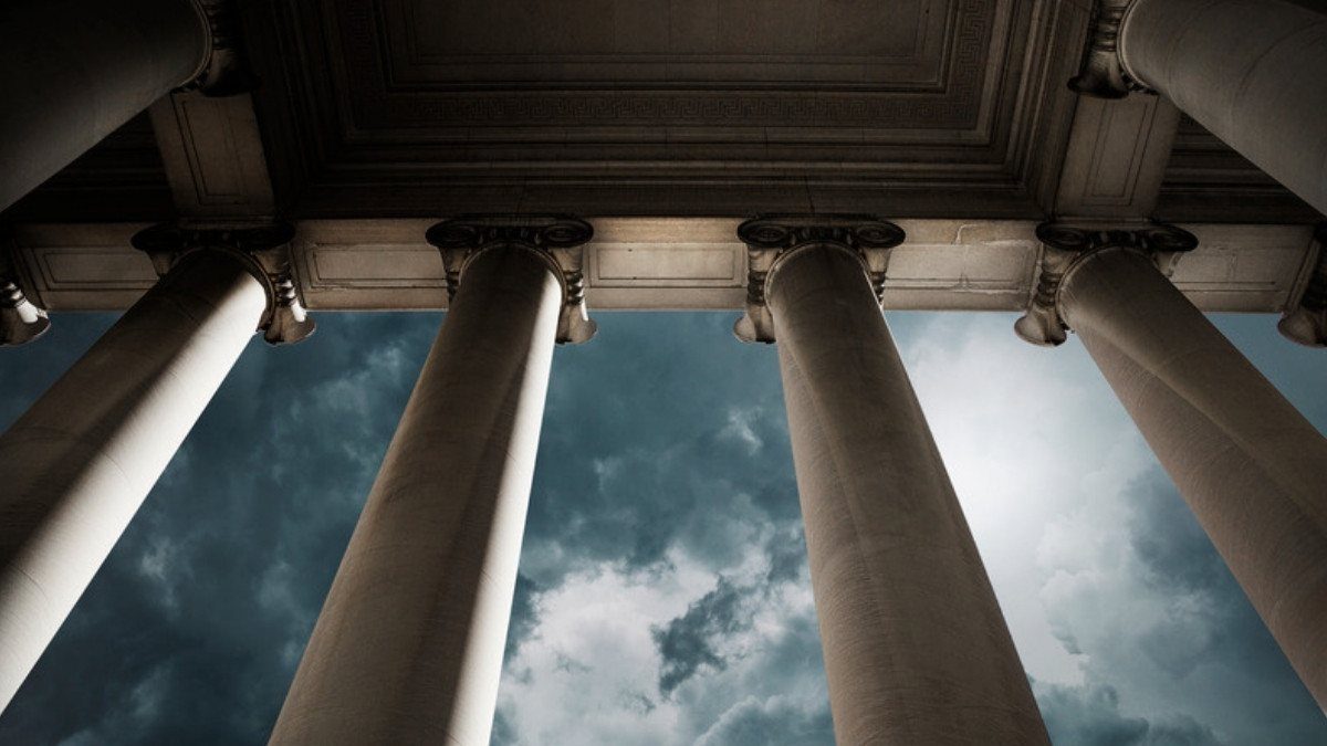 Tall stone columns frame a cloudy sky beneath the portico of a classical government building