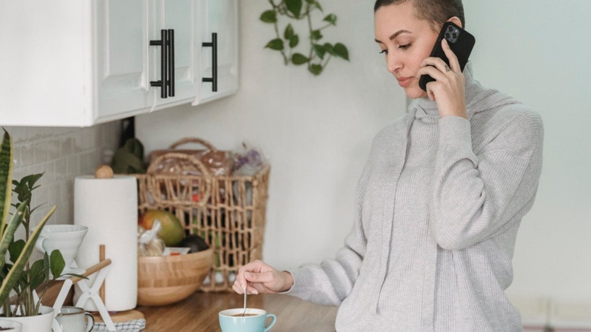 A woman stirs her coffee while talking on her phone in a bright kitchen, ready to reach personal injury attorneys in Orangeburg County