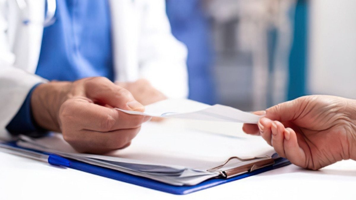 Discharge paperwork passes from a doctor's hands to a patient across a white desk with a blue clipboard