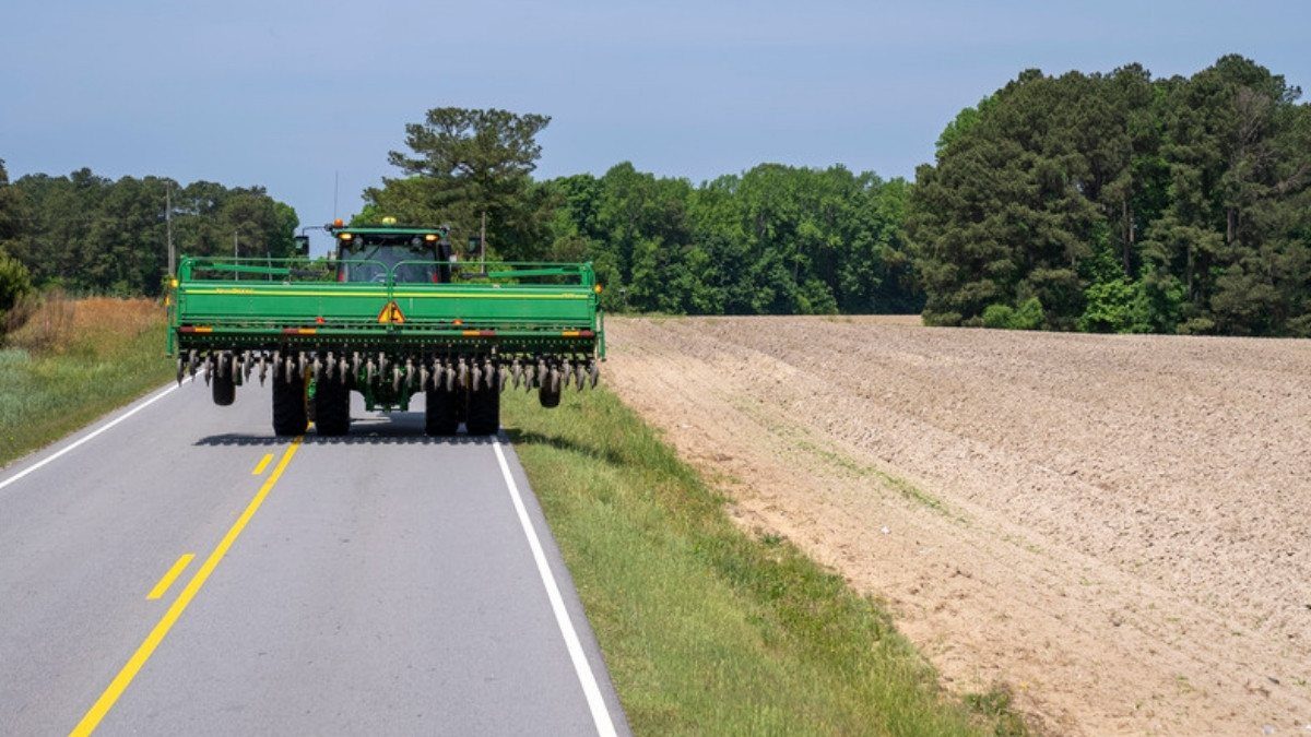 A farm tractor travels a two lane road beside a plowed field, a rural hazard personal injury attorneys in Williamsburg County know