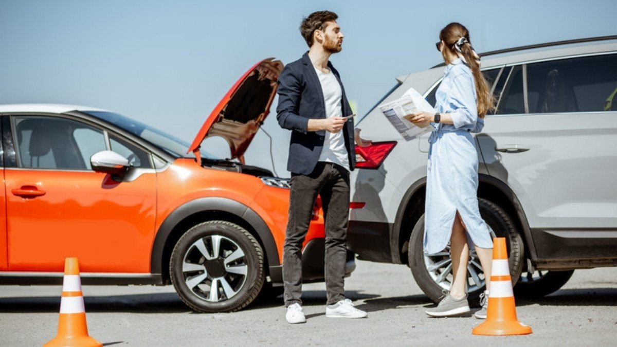 Two drivers talk beside an orange car and a white SUV with traffic cones set out after a crash on an open road