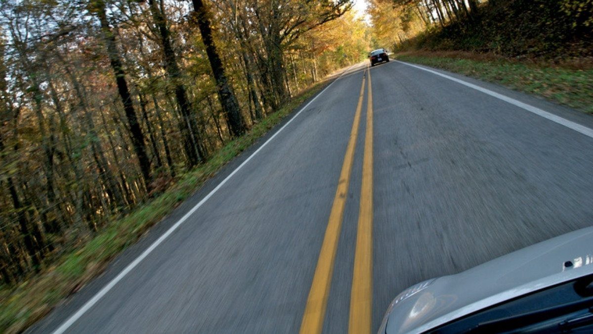A car drives a two lane road through autumn woods, and South Carolina personal injury attorneys see rural crashes on roads like it