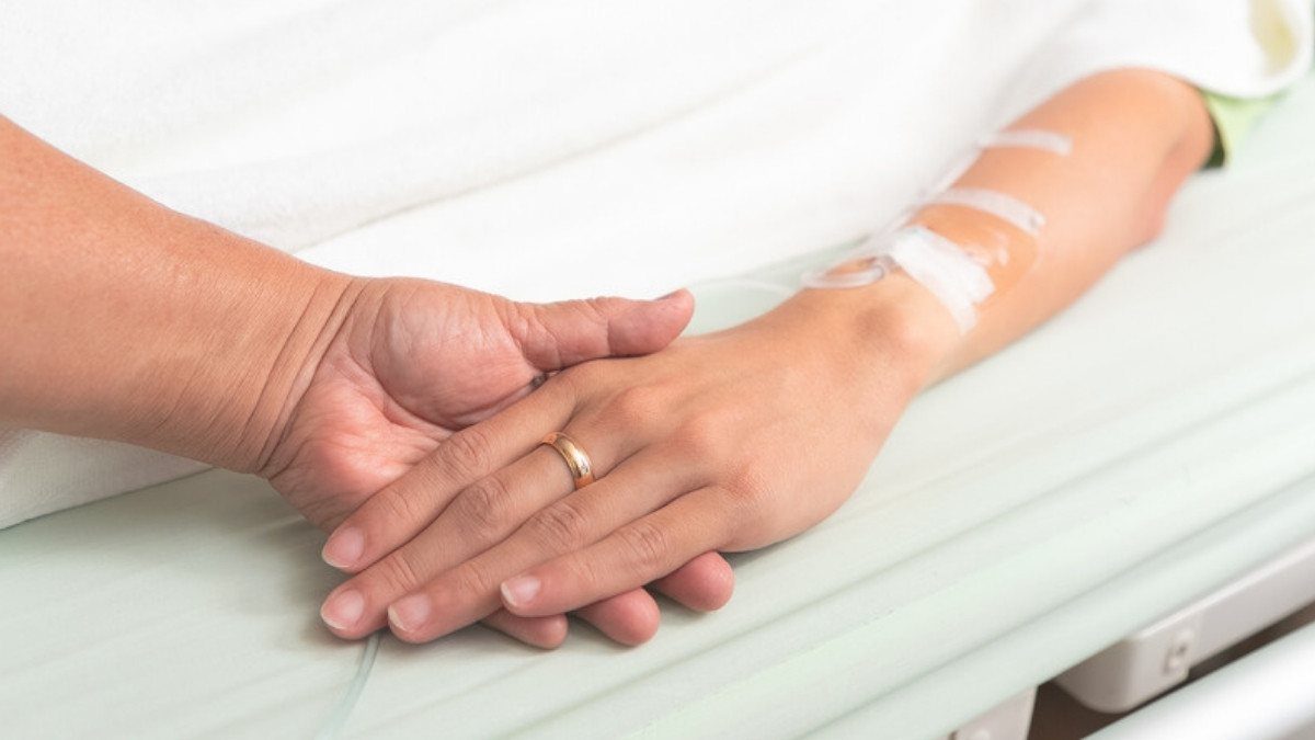A hand rests on a patient's hand beside an IV line in a hospital bed, the time in care survival action lawyers in Summerville document