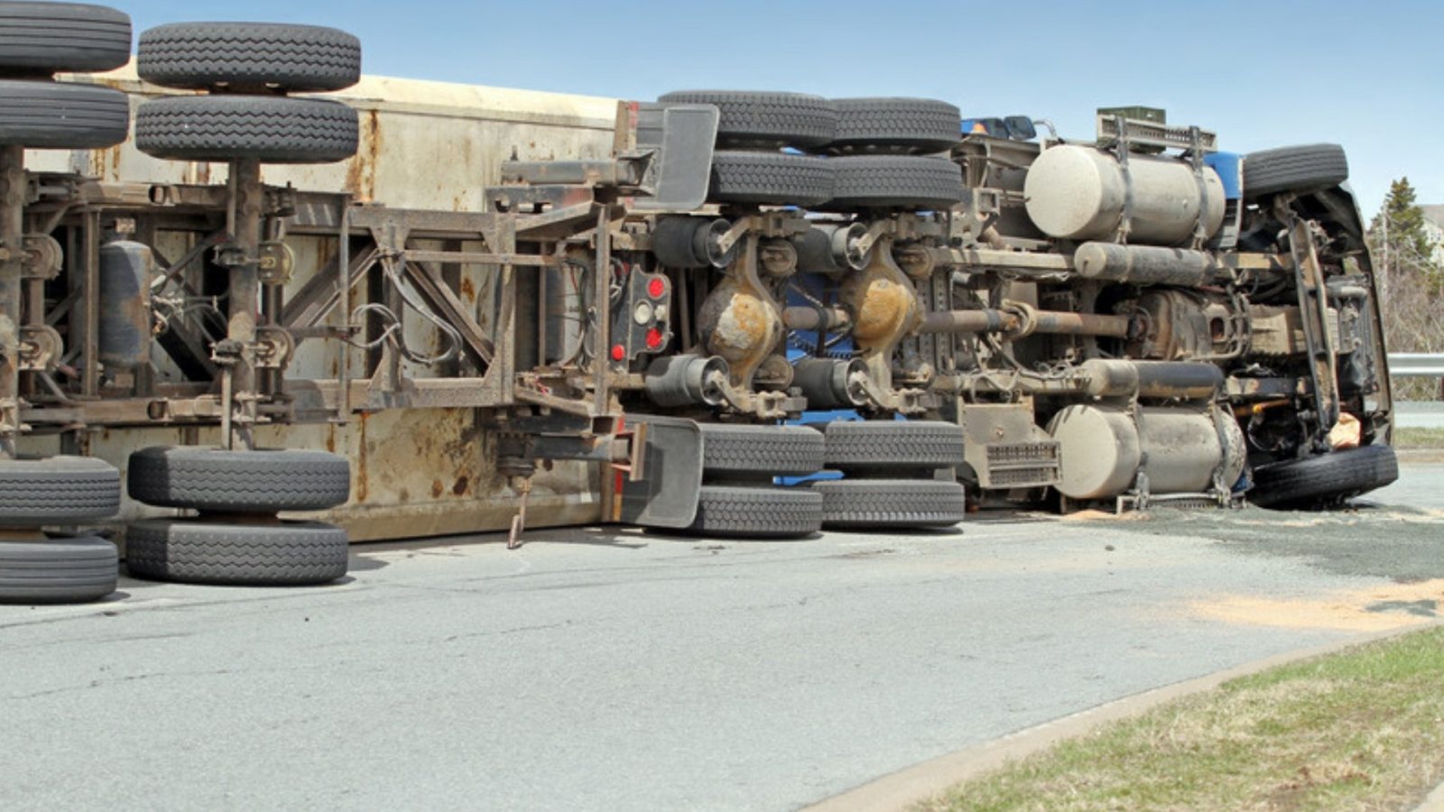 An overturned tractor-trailer lies on its side across a curving highway ramp.