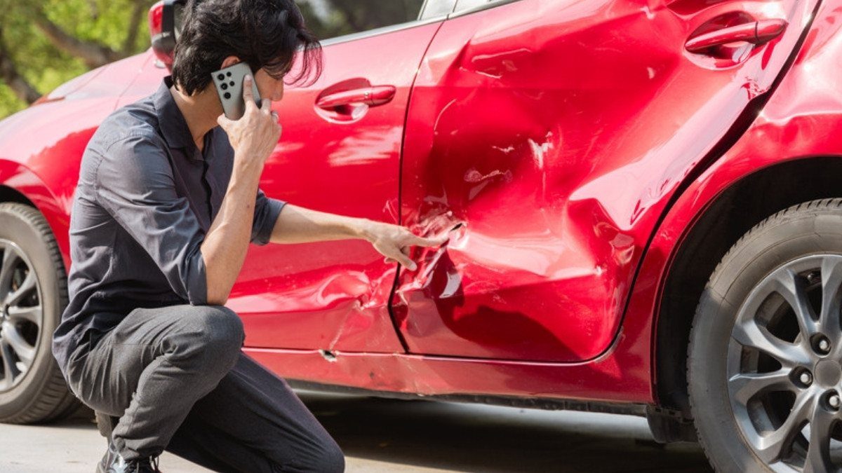 A driver on the phone points at a dented car door, damage uninsured motorist coverage can address when the other driver has no policy