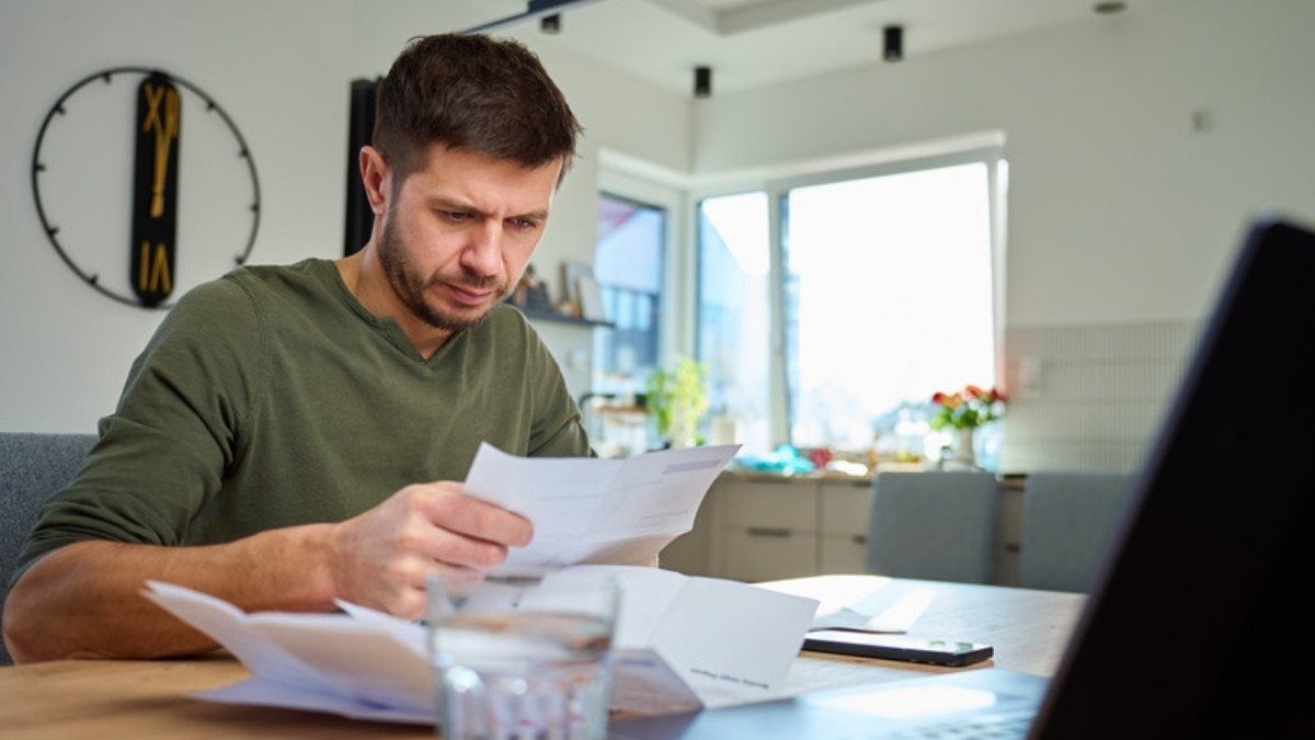A man reads through papers at his kitchen table, checking what his uninsured motorist coverage includes before he makes a call