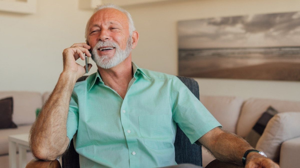 An older man laughs while talking on the phone in an armchair at home, one easy way to reach Walterboro car accident lawyers