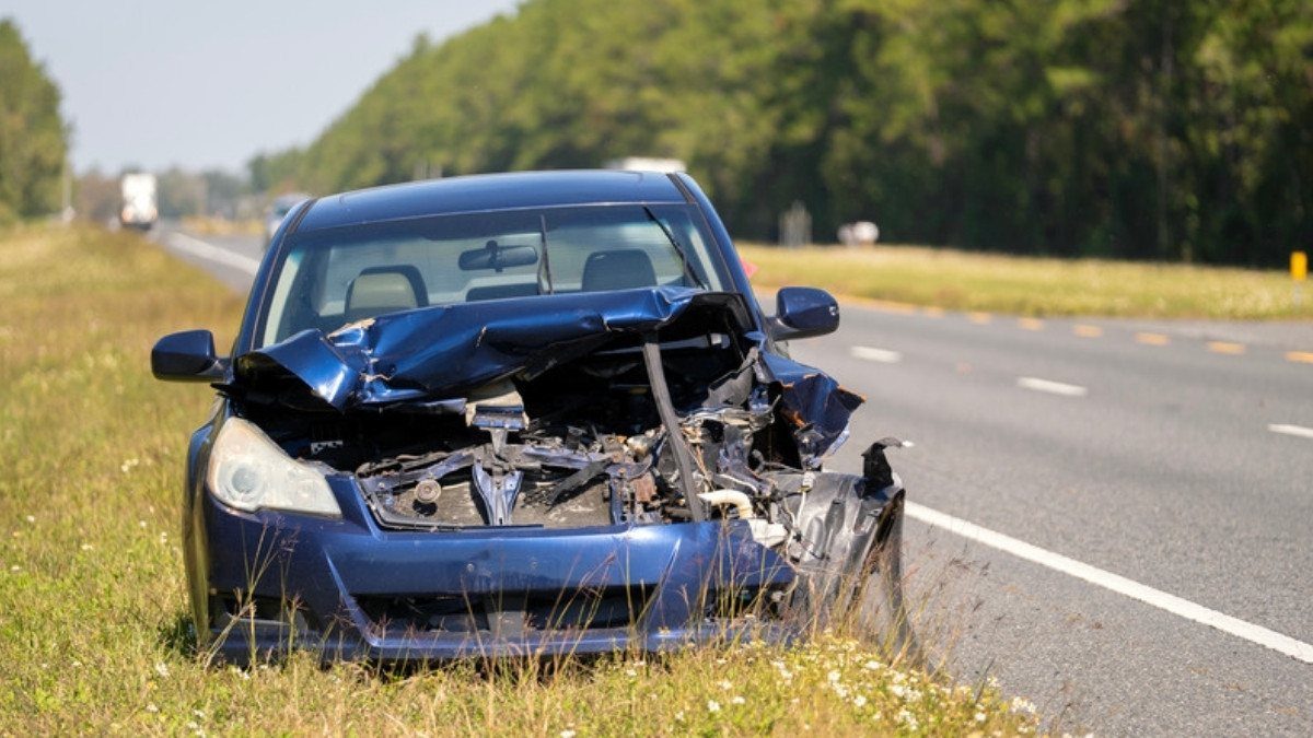 A wrecked sedan with a crushed front end sits on the grassy shoulder of a divided highway, a scene Walterboro car accident lawyers know