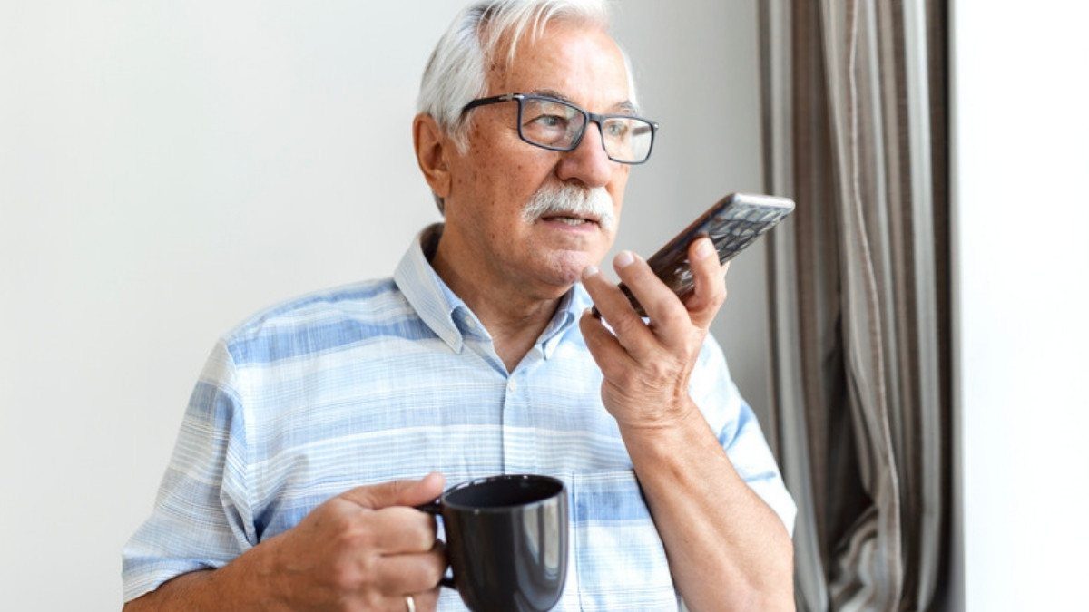 An older man holds a coffee mug and speaks on the phone by a window, a calm call to make even when a crash was your fault