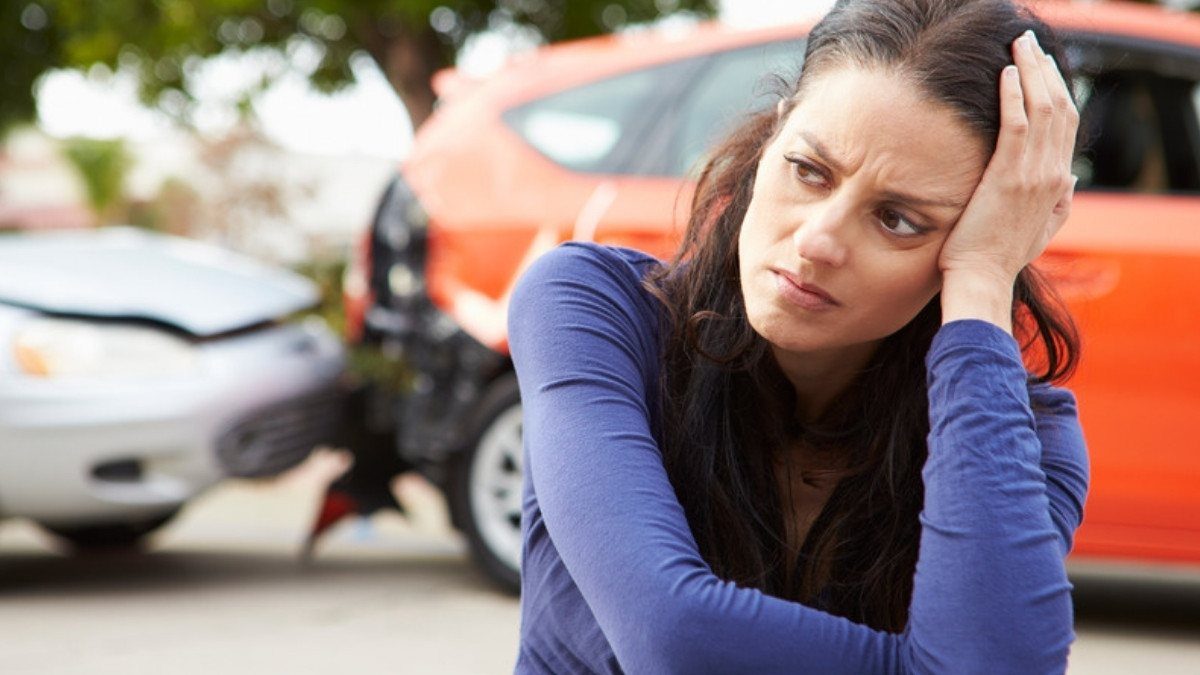 A worried driver sits beside two damaged cars with a hand on her head, a scene that raises questions if the crash was your fault