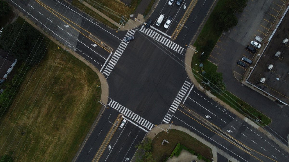 Turn lanes and crosswalks meet at a busy suburban intersection seen from above, the kind of crossing where car accidents cluster