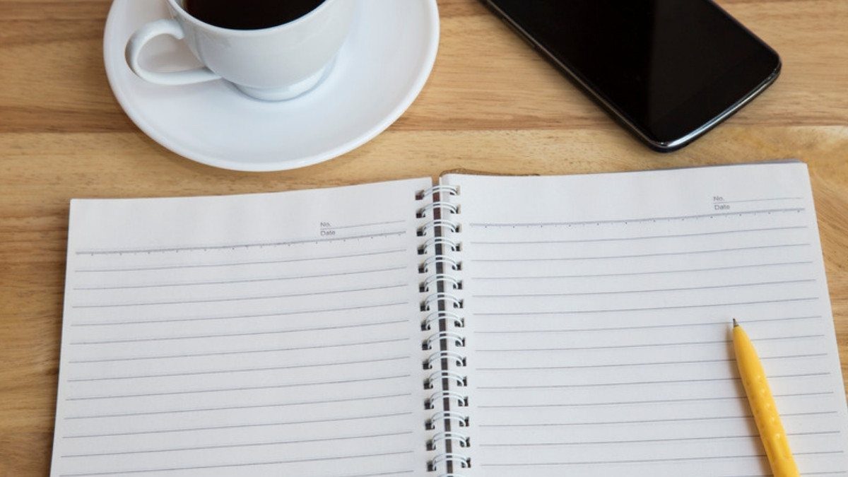 A blank notebook, yellow pencil, smartphone and cup of coffee wait on a wooden table, ready for a family to jot down questions